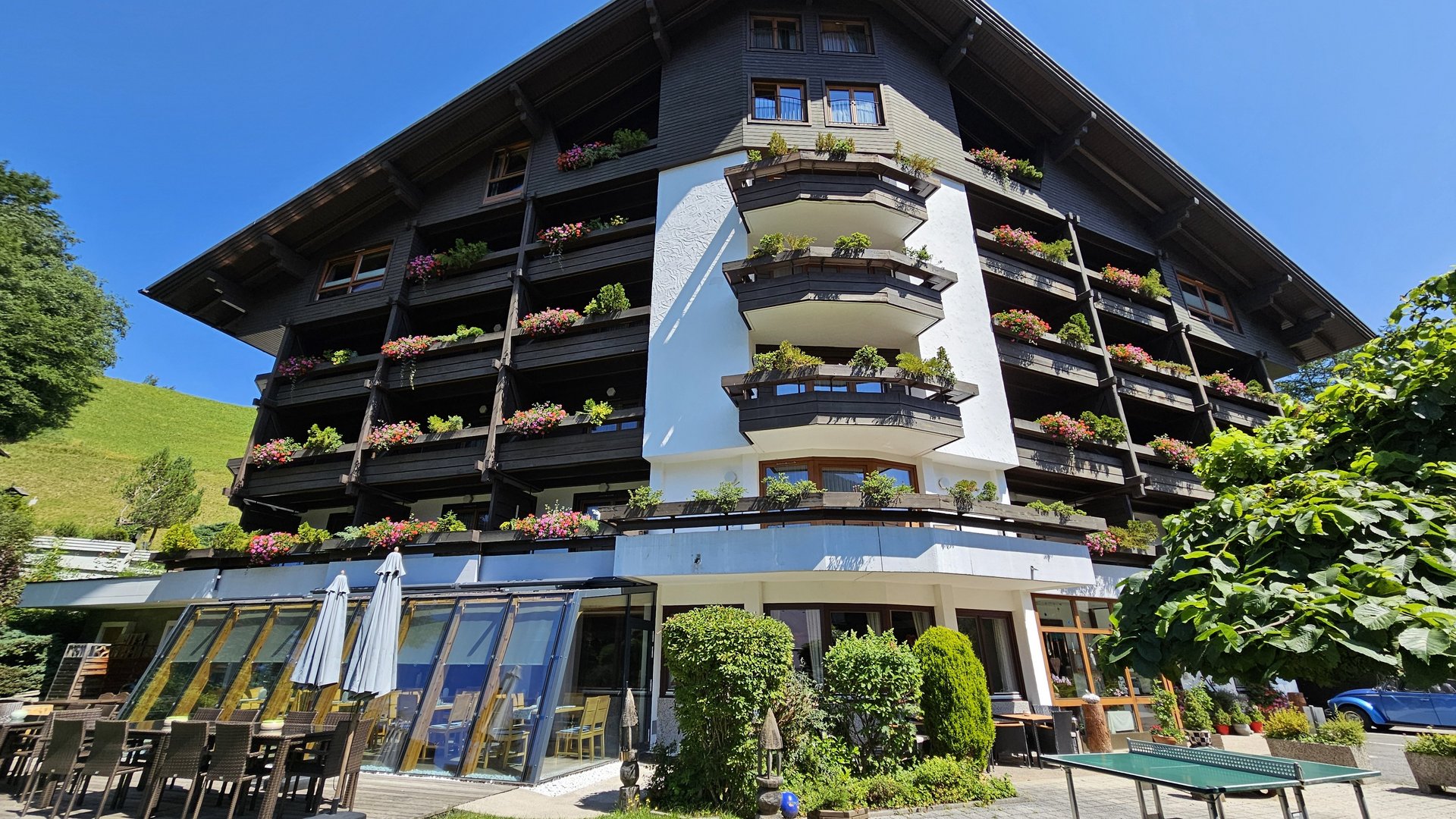 Traditionelles Alpenhotel Hotel mit traditioneller Architektur, farbenfrohen Blumen und sonniger Terrasse in Berglandschaft.